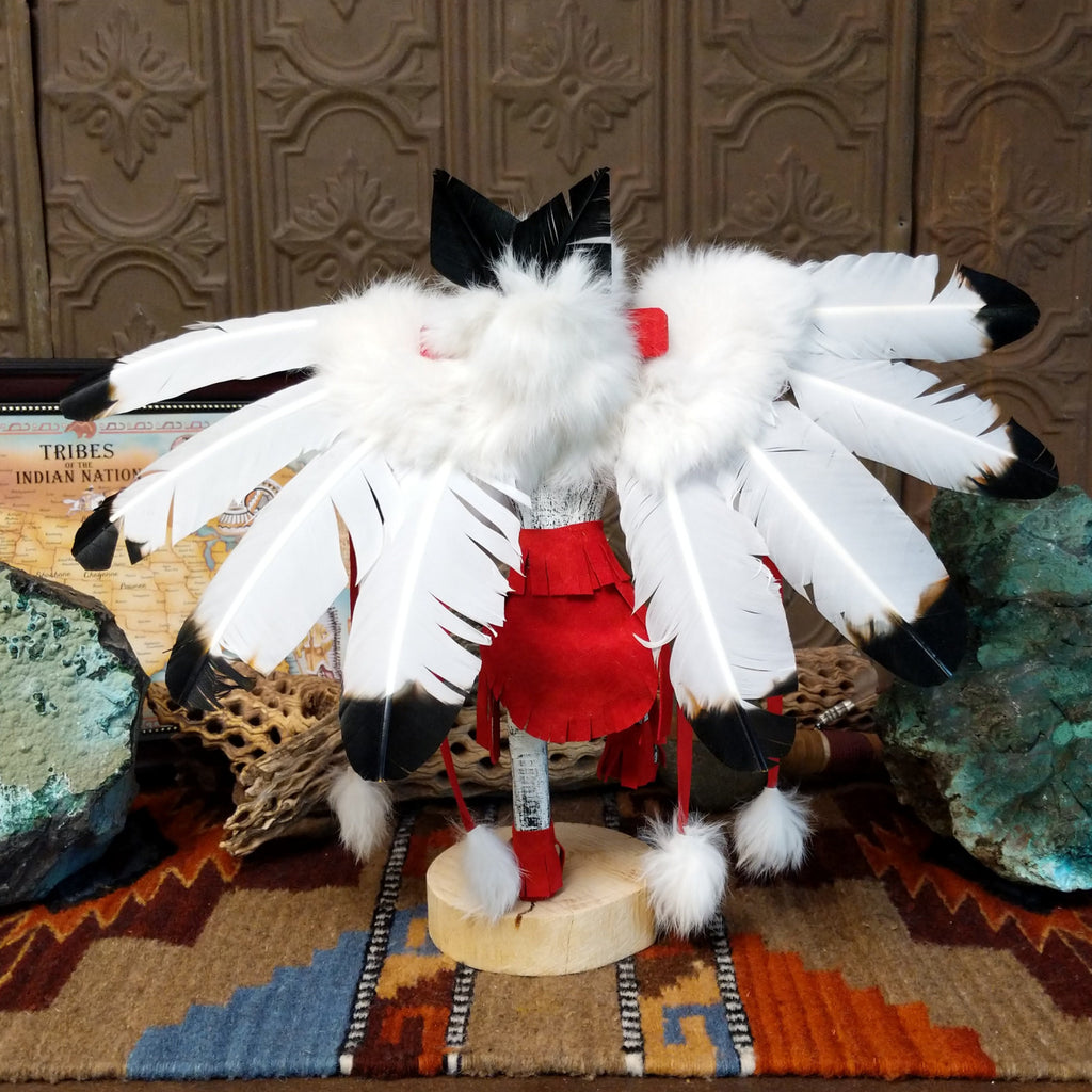 Wood carved into an eagle kachina with vibrant paints, feathers, and red suede clothing.