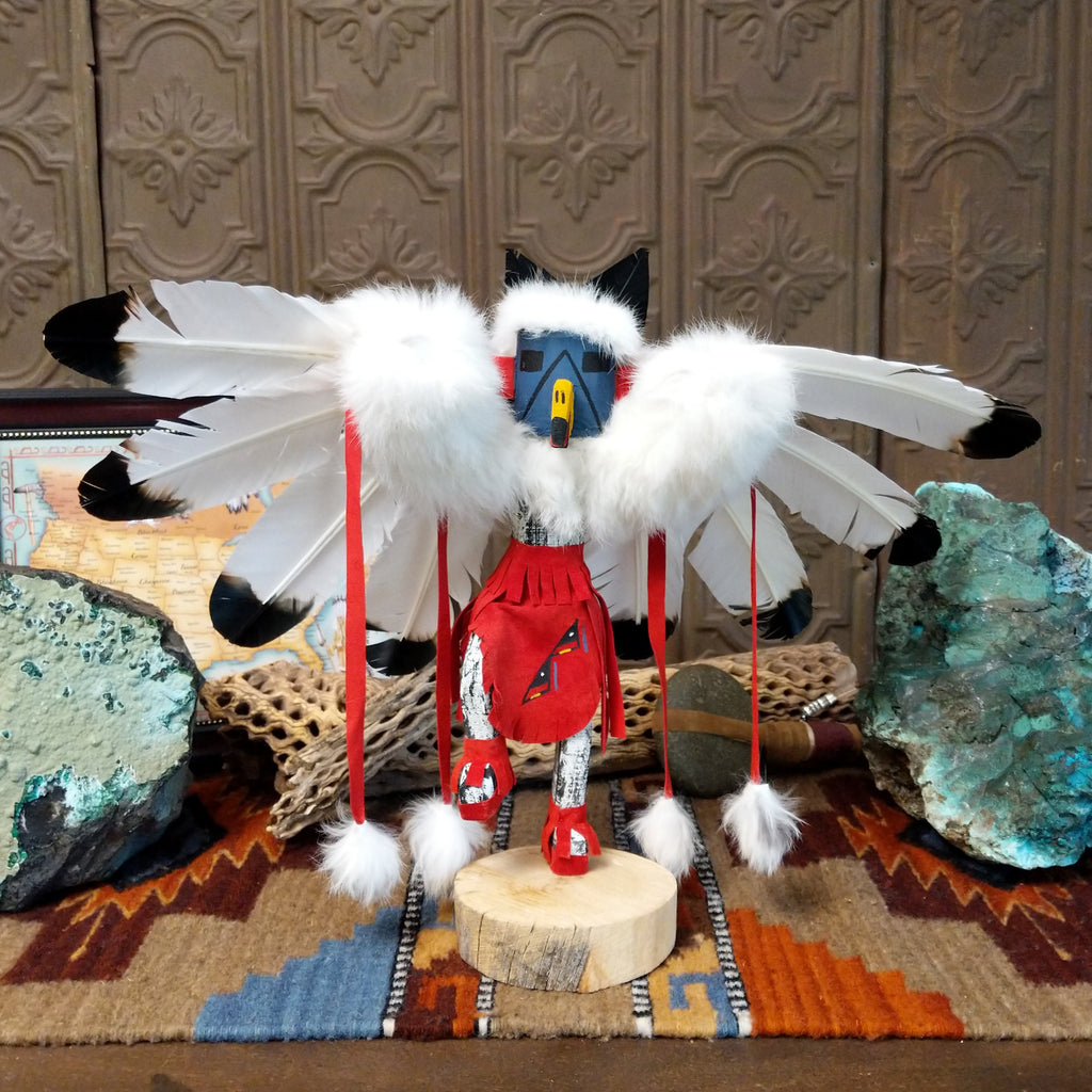 Wood carved into an eagle kachina with vibrant paints, feathers, and red suede clothing.