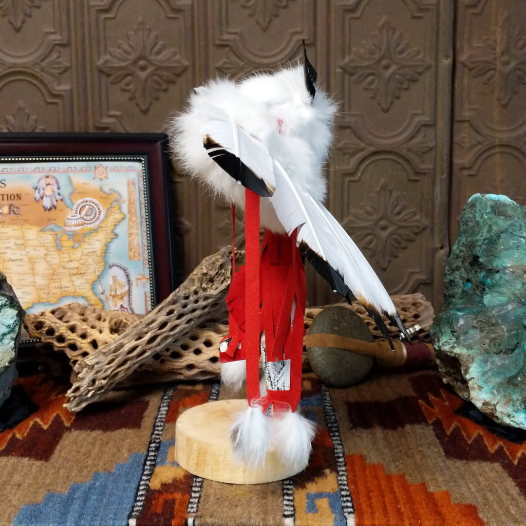 Wood carved into an eagle kachina with vibrant paints, feathers, and red suede clothing.