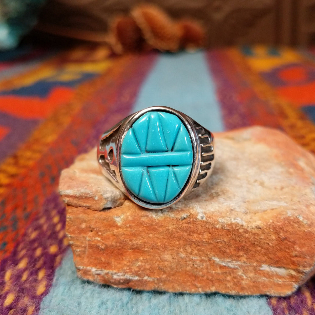 Navajo Etched Turquoise Ring featuring an oval turquoise stone carved with symmetrical geometric triangular patterns and a raised horizontal bar, set in a polished silver band with openwork side details.