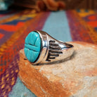 Navajo Etched Turquoise Ring featuring an oval turquoise stone carved with symmetrical geometric triangular patterns and a raised horizontal bar, set in a polished silver band with openwork side details; side view.