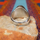 Navajo Etched Turquoise Ring featuring an oval turquoise stone carved with symmetrical geometric triangular patterns and a raised horizontal bar, set in a polished silver band with openwork side details; underside view.