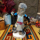 Back view of the Navajo Field House Kachina doll with oversized fur headdress, painted white face, blue sleeves, and outstretched arms.