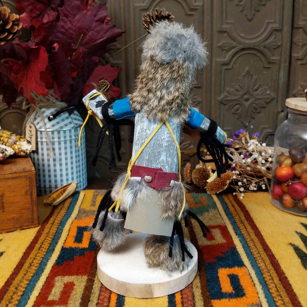 Back view of the Navajo Field House Kachina doll with oversized fur headdress, painted white face, blue sleeves, and outstretched arms.