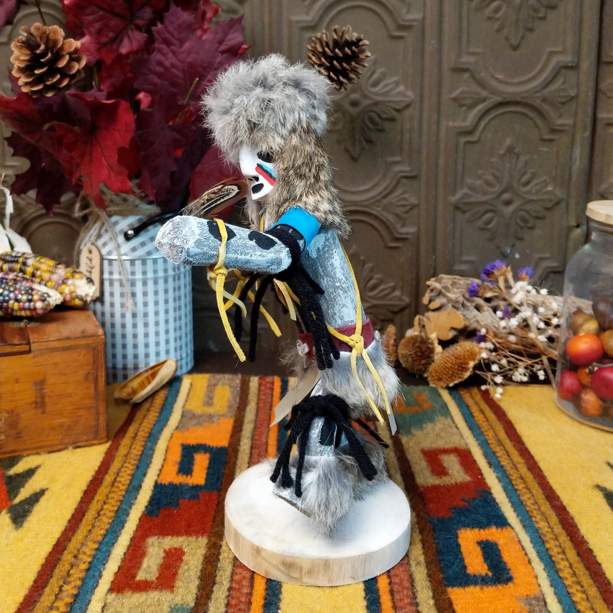 Side view of the Navajo Field House Kachina doll with oversized fur headdress, painted white face, blue sleeves, and outstretched arms.