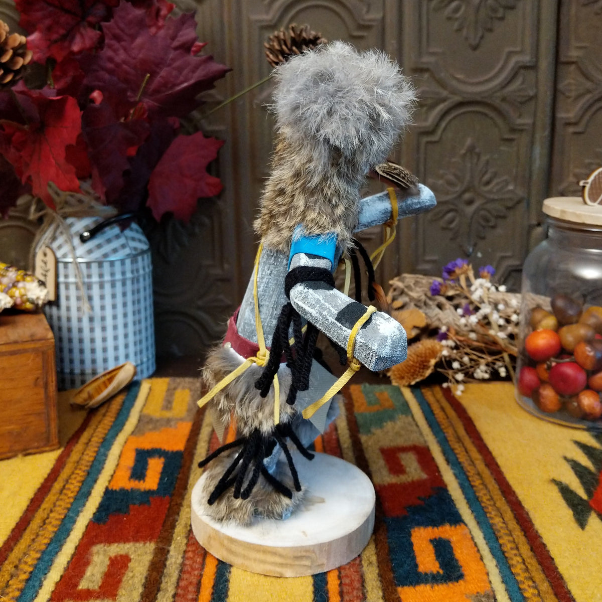 Side view of the Navajo Field House Kachina doll with oversized fur headdress, painted white face, blue sleeves, and outstretched arms.