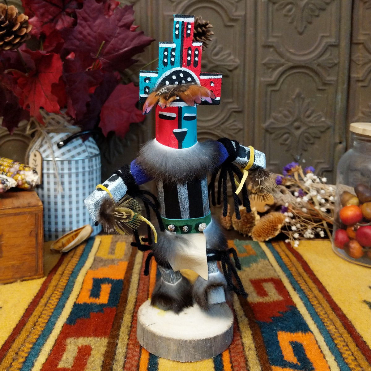 This vibrant Navajo Hemis Kachina by Debbie James features a hand-painted red and turquoise mask, stepped headdress, natural feathers, soft fur accents, leather ties, and a circular wooden display base.