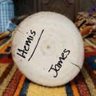 This vibrant Navajo Hemis Kachina by Debbie James features a hand-painted red and turquoise mask, stepped headdress, natural feathers, soft fur accents, leather ties, and a circular wooden display base; artisan and product name on bottom.