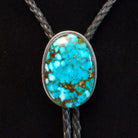 Navajo Kingman Turquoise Bolo Tie featuring a large oval sky-blue turquoise stone with golden-brown matrix, decorative silver bezel, braided black leather cord, and polished silver tips; close up view of stone.
