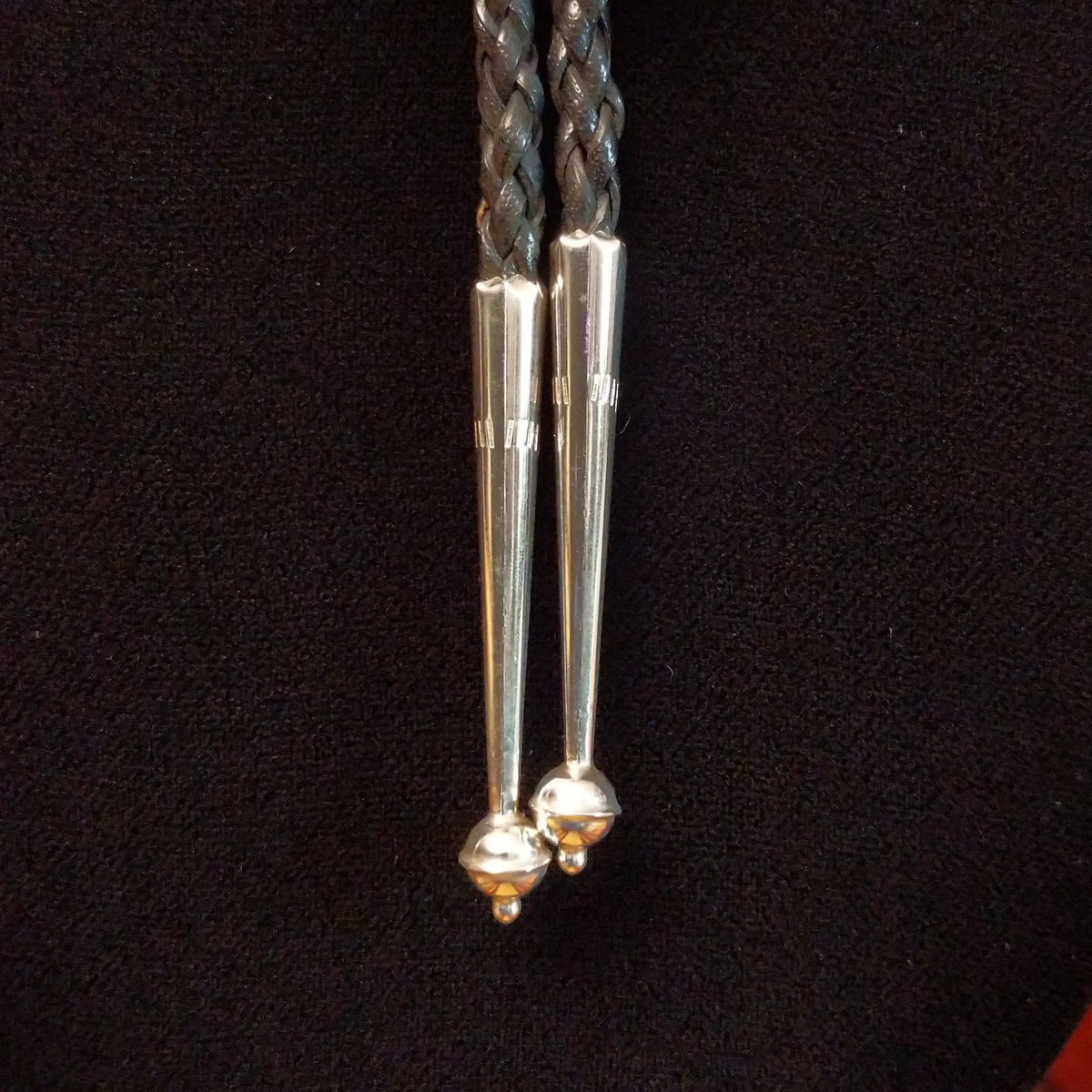 Navajo Kingman Turquoise Bolo Tie featuring a large oval sky-blue turquoise stone with golden-brown matrix, decorative silver bezel, braided black leather cord, and polished silver tips; close up view of tips.