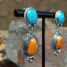 Handcrafted sterling silver Navajo Kingman turquoise and orange spiny oyster earrings, featuring a two-stone dangle design with traditional rope and stamped silver details; side view.