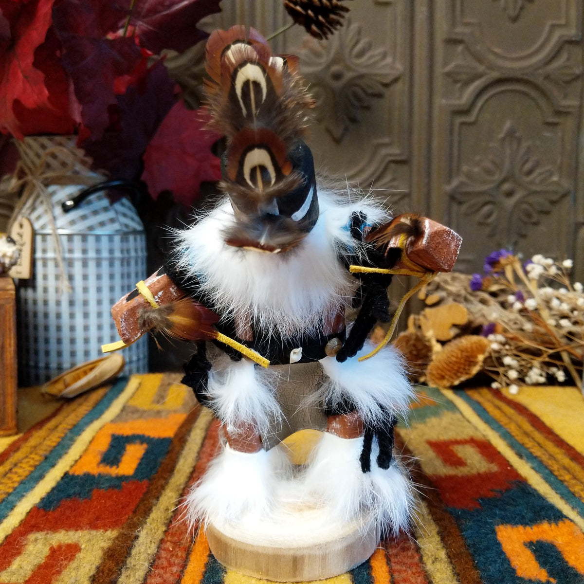 This distinctive Navajo Kokopelli Kachina by Debbie James features a hand-painted wooden figure with a tall feather headdress, black face, white fur accents, natural feathers, leather ties, and a wooden display base.