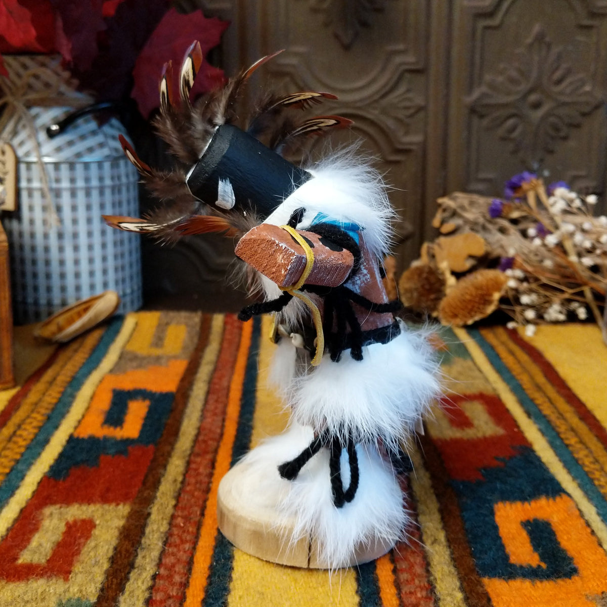 This distinctive Navajo Kokopelli Kachina by Debbie James features a hand-painted wooden figure with a tall feather headdress, black face, white fur accents, natural feathers, leather ties, and a wooden display base; side view.