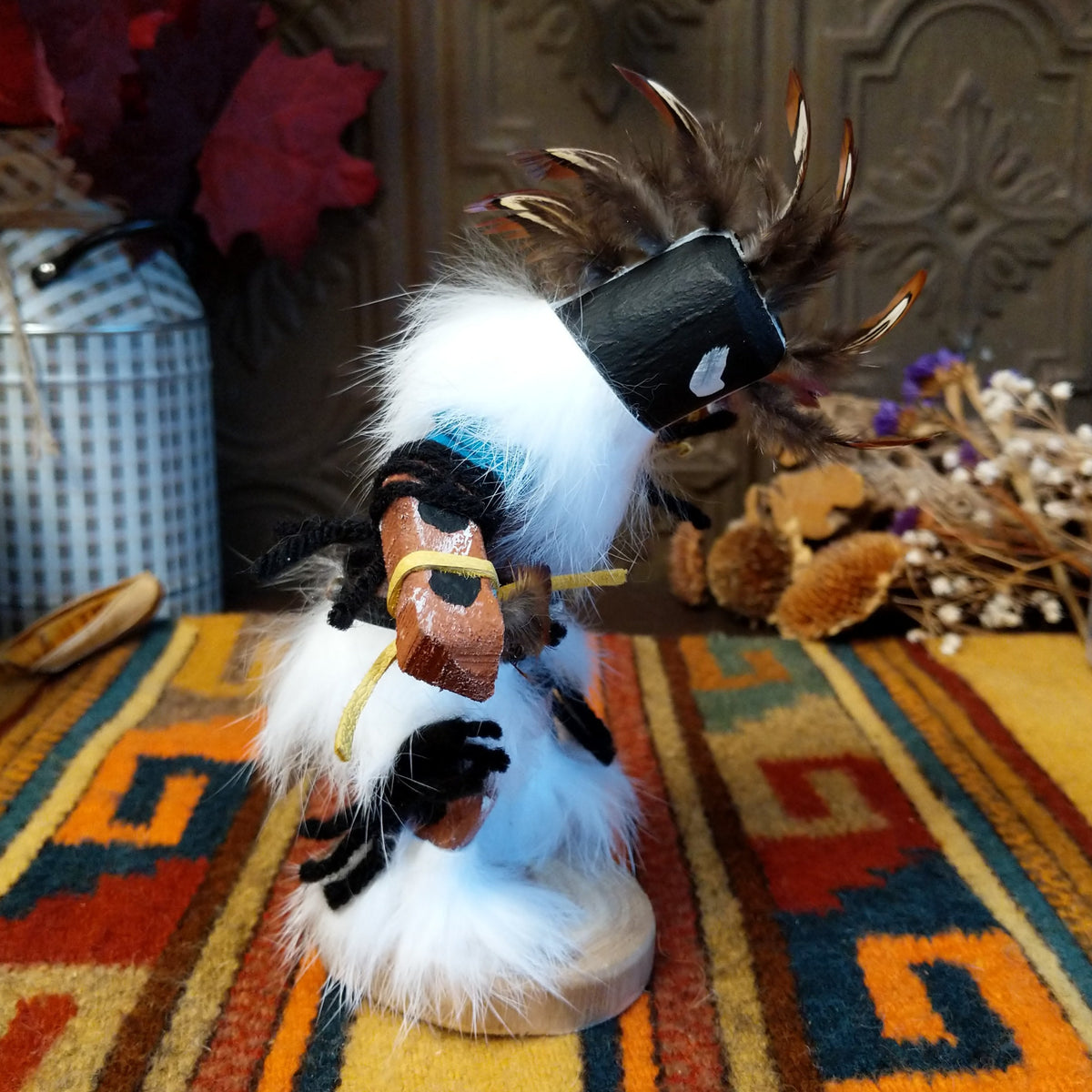 This distinctive Navajo Kokopelli Kachina by Debbie James features a hand-painted wooden figure with a tall feather headdress, black face, white fur accents, natural feathers, leather ties, and a wooden display base; side view.