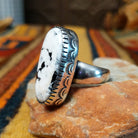 Navajo Large White Buffalo Ring featuring an elongated oval white stone with bold black matrix patterns, surrounded by a decorative notched silver bezel in a classic Southwestern statement design; side view.