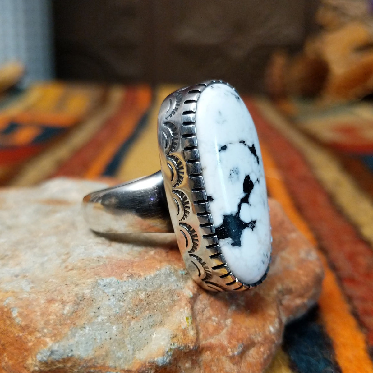 Navajo Large White Buffalo Ring featuring an elongated oval white stone with bold black matrix patterns, surrounded by a decorative notched silver bezel in a classic Southwestern statement design; side view.