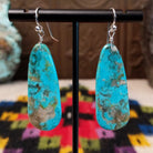 Navajo Long Oval Slab Turquoise Earrings featuring elongated bright blue turquoise stones with natural brown, gray, and green matrix, suspended from silver hooks.