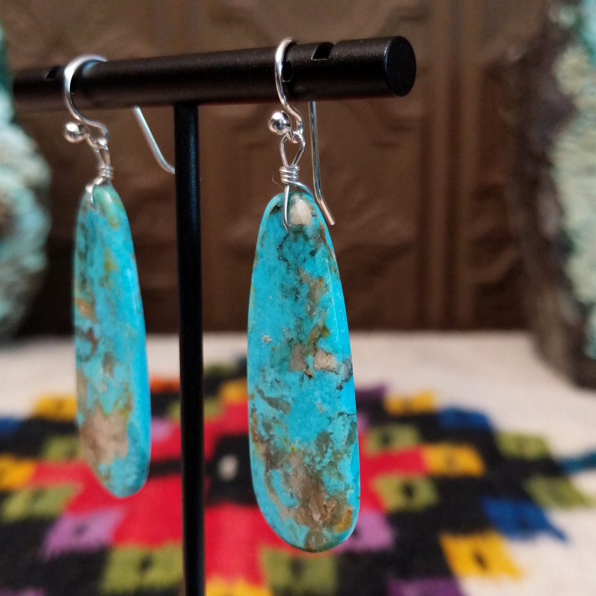 Navajo Long Oval Slab Turquoise Earrings featuring elongated bright blue turquoise stones with natural brown, gray, and green matrix, suspended from silver hooks; side view.