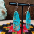 Navajo Long Oval Slab Turquoise Earrings featuring elongated bright blue turquoise stones with natural brown, gray, and green matrix, suspended from silver hooks; side view.
