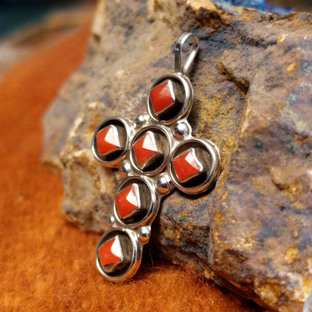 Coral set in sterling silver bezels on a cross with dotted accents.