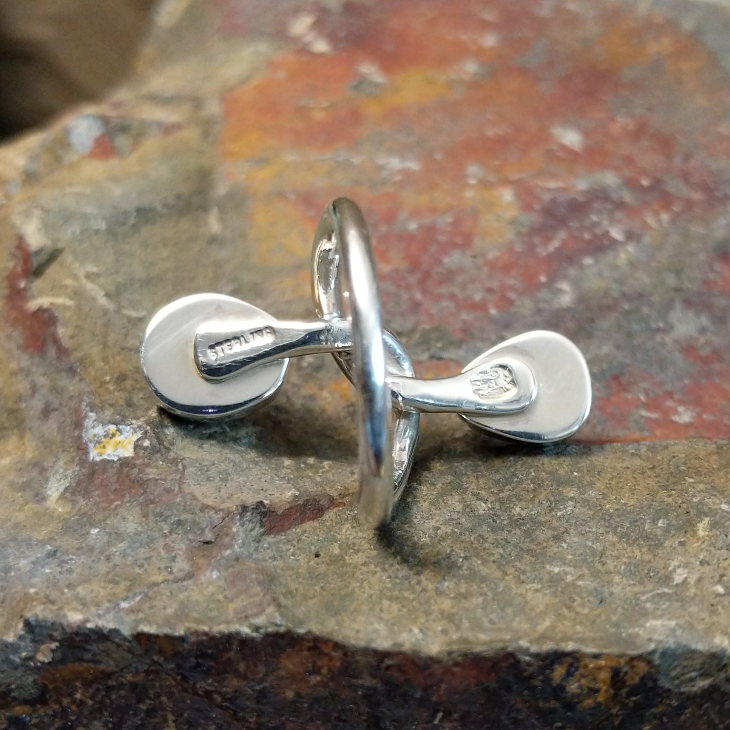 Silver ring with entwined band on the inner side, no stones visible. Smooth silver finish on the band with sterling silver stamped.