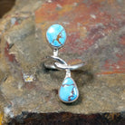 Silver ring with entwined band holding an oval turquoise stone and a teardrop turquoise stone in smooth bezels. Matrix veining visible in both stones.