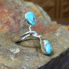 Silver ring with entwined band curving around an oval turquoise stone and teardrop turquoise stone. Smooth bezel settings highlight the stones.