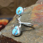 Silver ring with entwined band curving around an oval turquoise stone and teardrop turquoise stone. Smooth bezel settings highlight the stones.