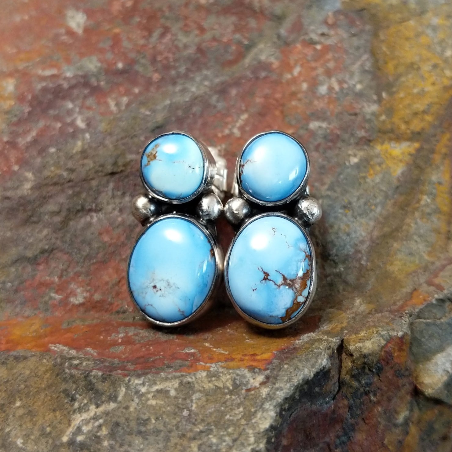 The Navajo made golden hills turquoise earrings by J.D. feature two round turquoise stones per earring, their brown matrix vibrant against a simple silver bezel. Small silver beads add a touch of Navajo artistry between the stones.