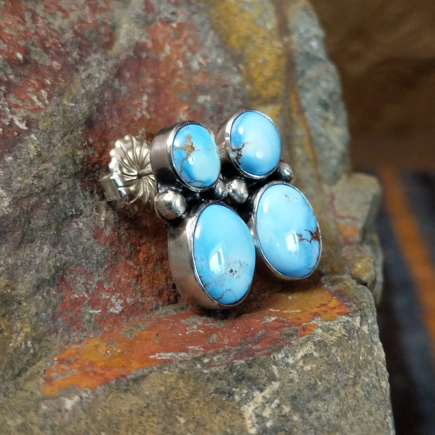 A side view of the navajo made golden hills turquoise earrings by J.D. shows the smooth edge of the turquoise stones in a simple bezel. The silver post gleams subtly against the stone’s bright blue.