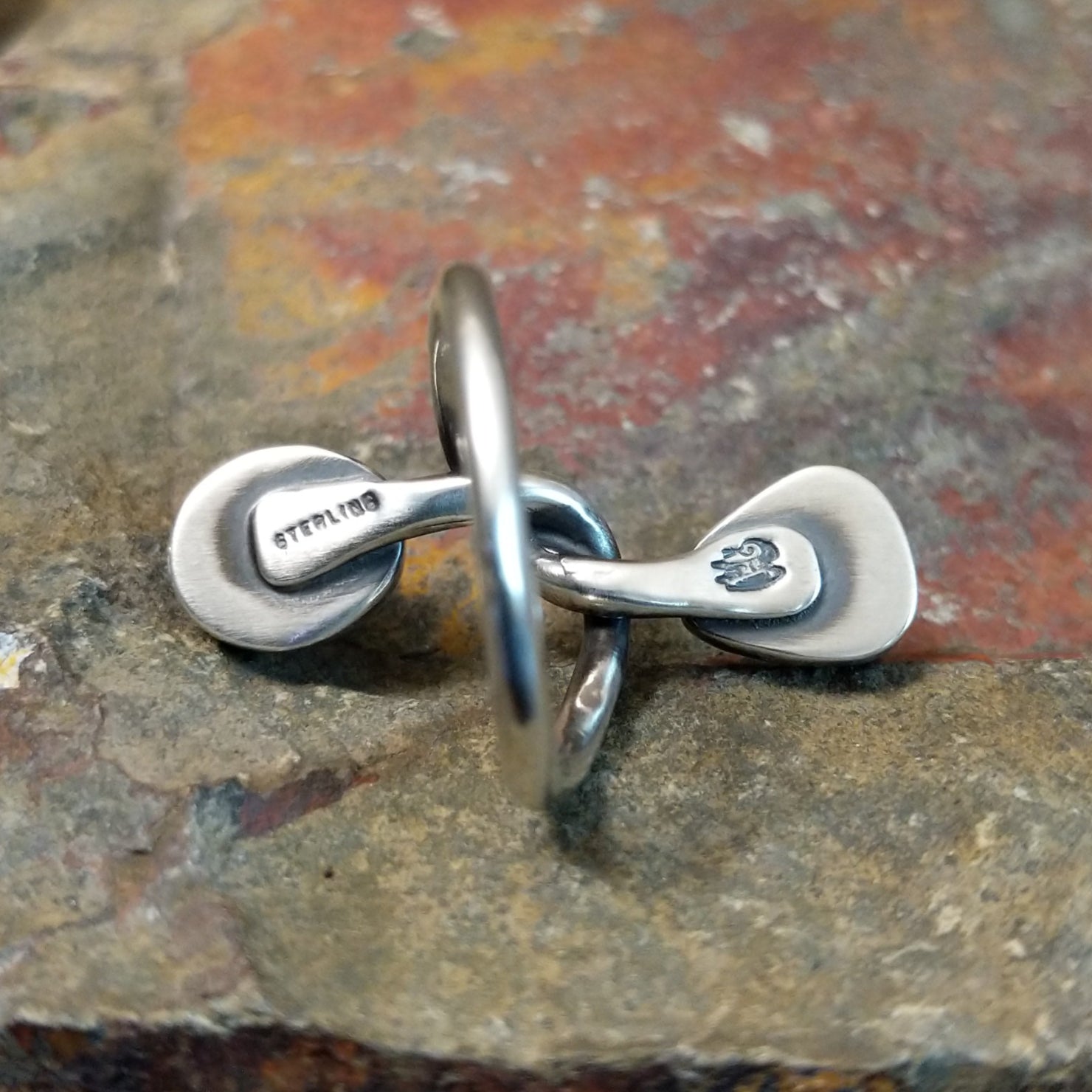 Silver ring with entwined band on the inner side, no stones visible. Smooth silver finish with stamp.