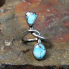 Silver ring with entwined band and a triangular turquoise stone plus an oval turquoise stone in smooth bezels. Matrix veining patterns across both stones.