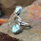 Silver ring with entwined band curving around a triangular turquoise stone and oval turquoise stone. Smooth bezel settings enhance the stones.