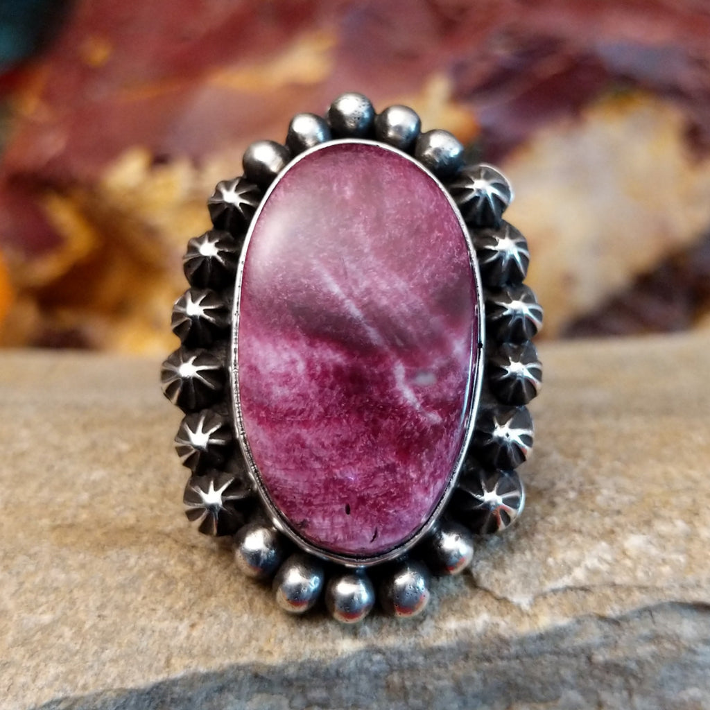 Star and dotted accents on the setting with an oval purple spiny oyster shell set inside it.