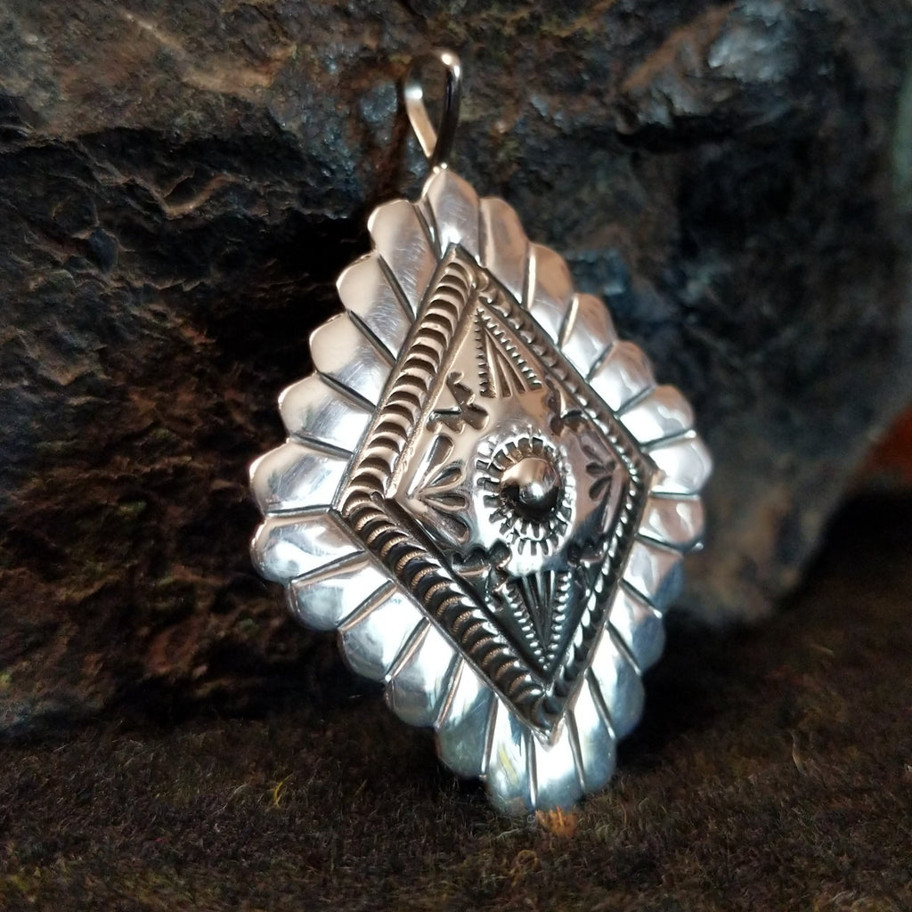 Stamped sterling silver pendant with scalloped edges and various designs.