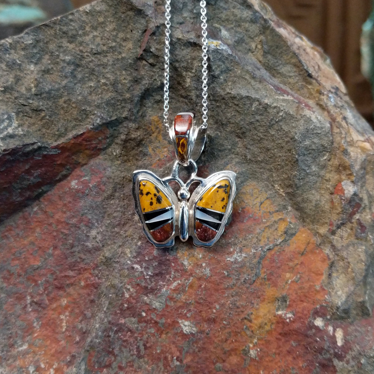 Navajo multistone butterfly pendant by K.S. featuring golden-yellow, reddish-brown, black, and white stone inlay set in polished silver butterfly wings.