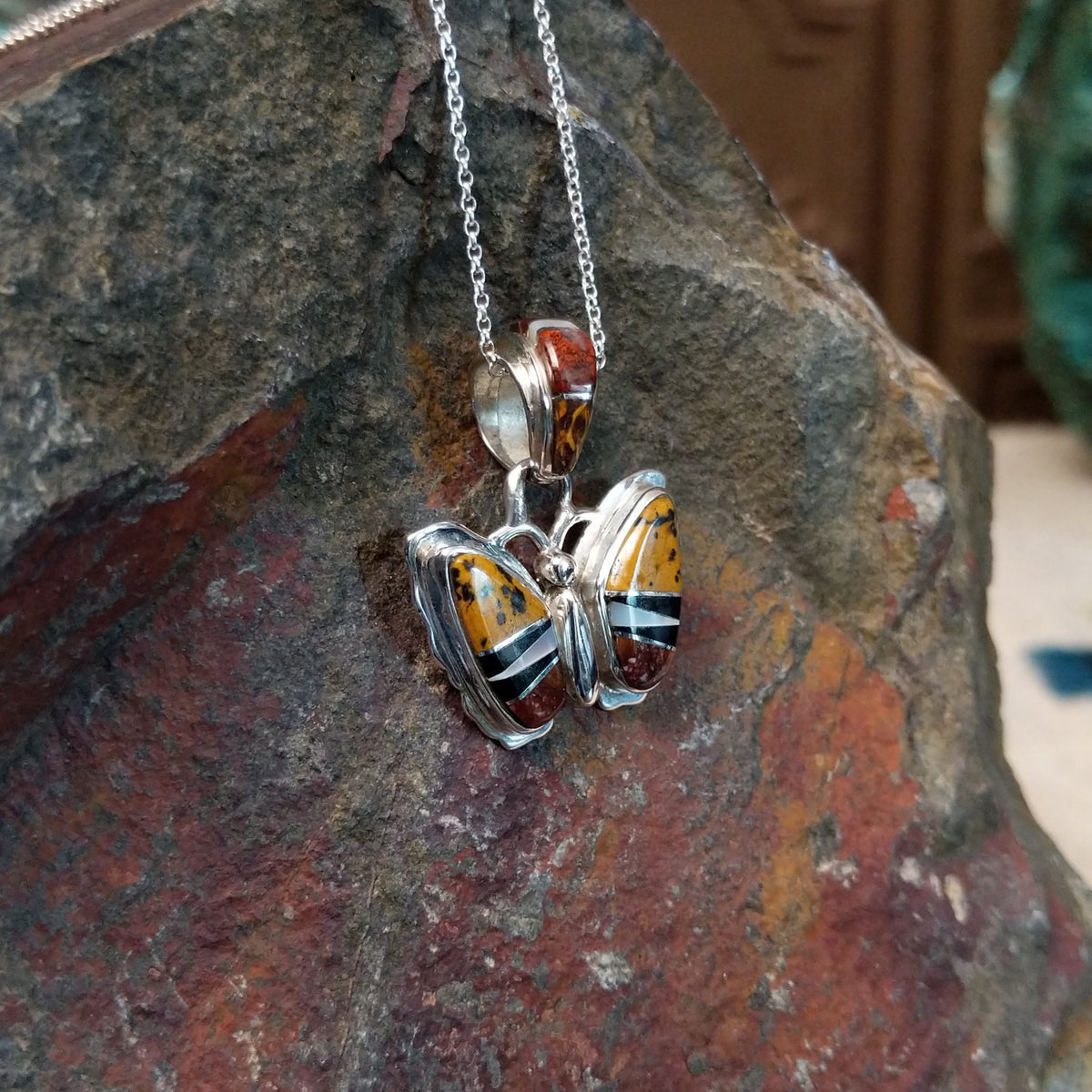 Navajo multistone butterfly pendant by K.S. featuring golden-yellow, reddish-brown, black, and white stone inlay set in polished silver butterfly wings; side view.