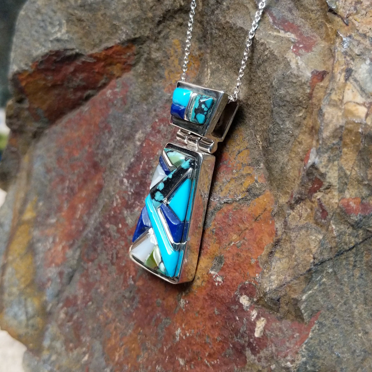 Navajo multistone cobblestone inlay pendant by J.Y. featuring turquoise, lapis, black matrix turquoise, white, and green stone inlay in a geometric sterling silver design; side view.