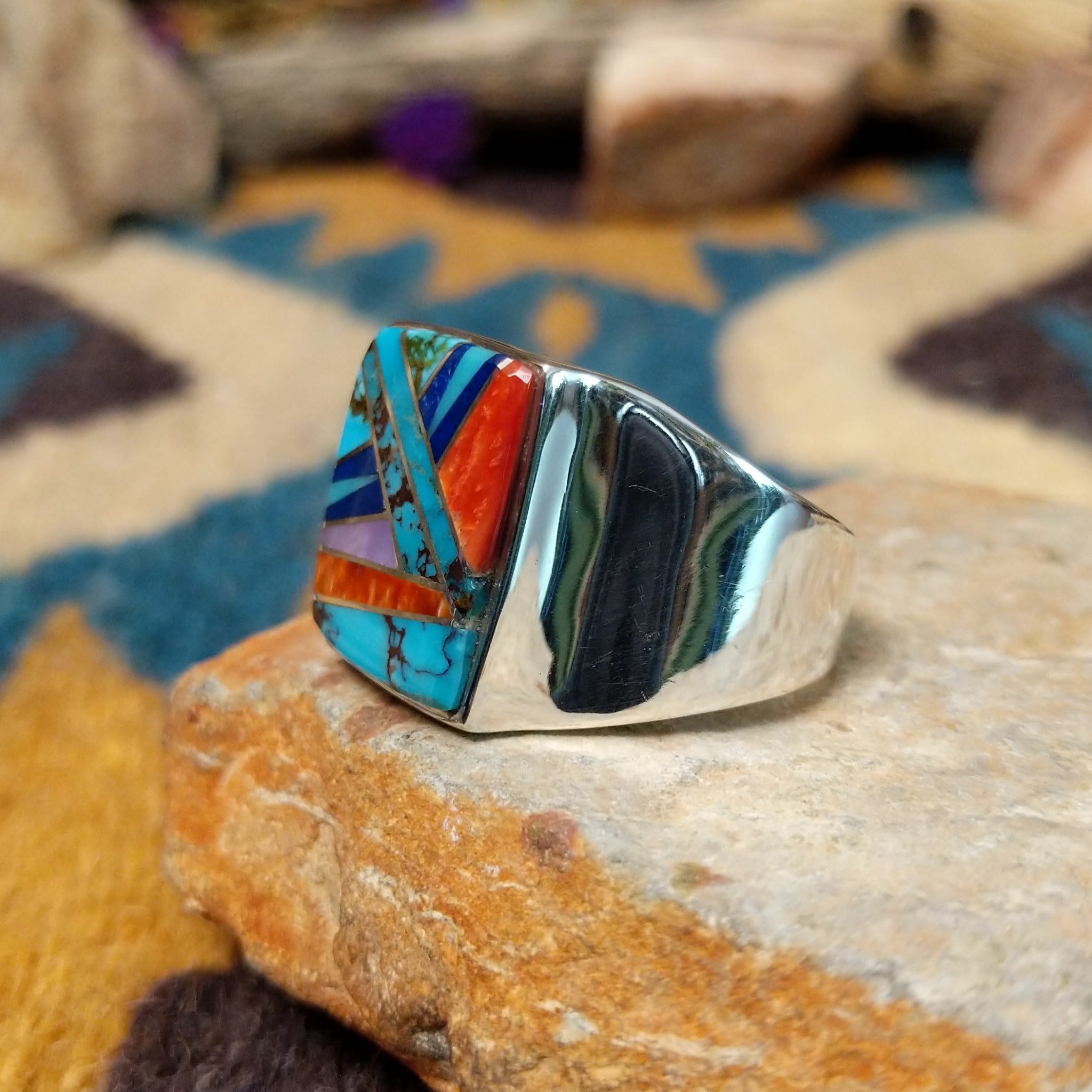 Sterling silver Navajo multistone inlay ring featuring turquoise, orange spiny oyster shell, lapis, and geometric mosaic inlay on a polished signet-style band; side view.
