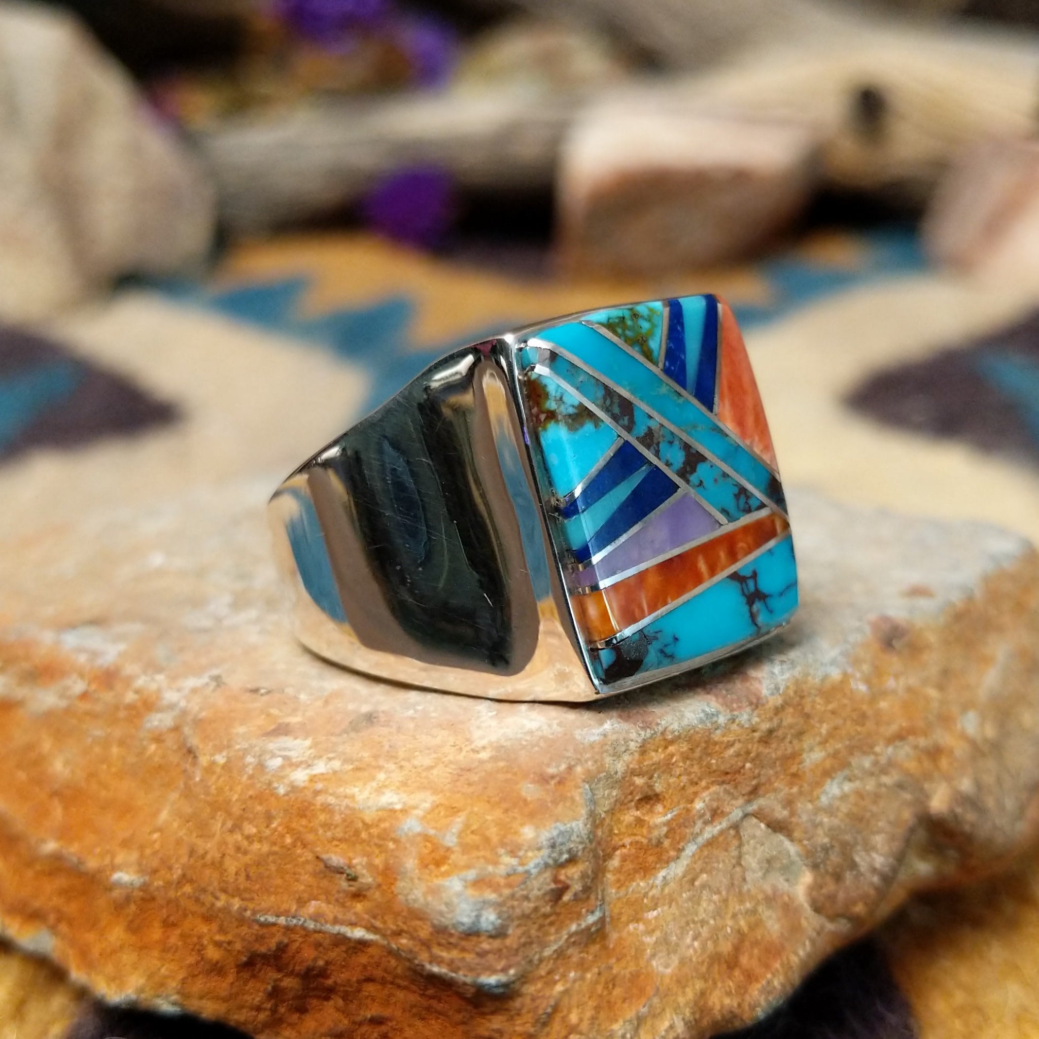 Sterling silver Navajo multistone inlay ring featuring turquoise, orange spiny oyster shell, lapis, and geometric mosaic inlay on a polished signet-style band; side view.