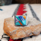 Navajo Multistone Inlay Ring by A.M.P. featuring a square geometric mosaic of turquoise, blue, purple, orange, red, and iridescent inlay set in a wide polished silver band.