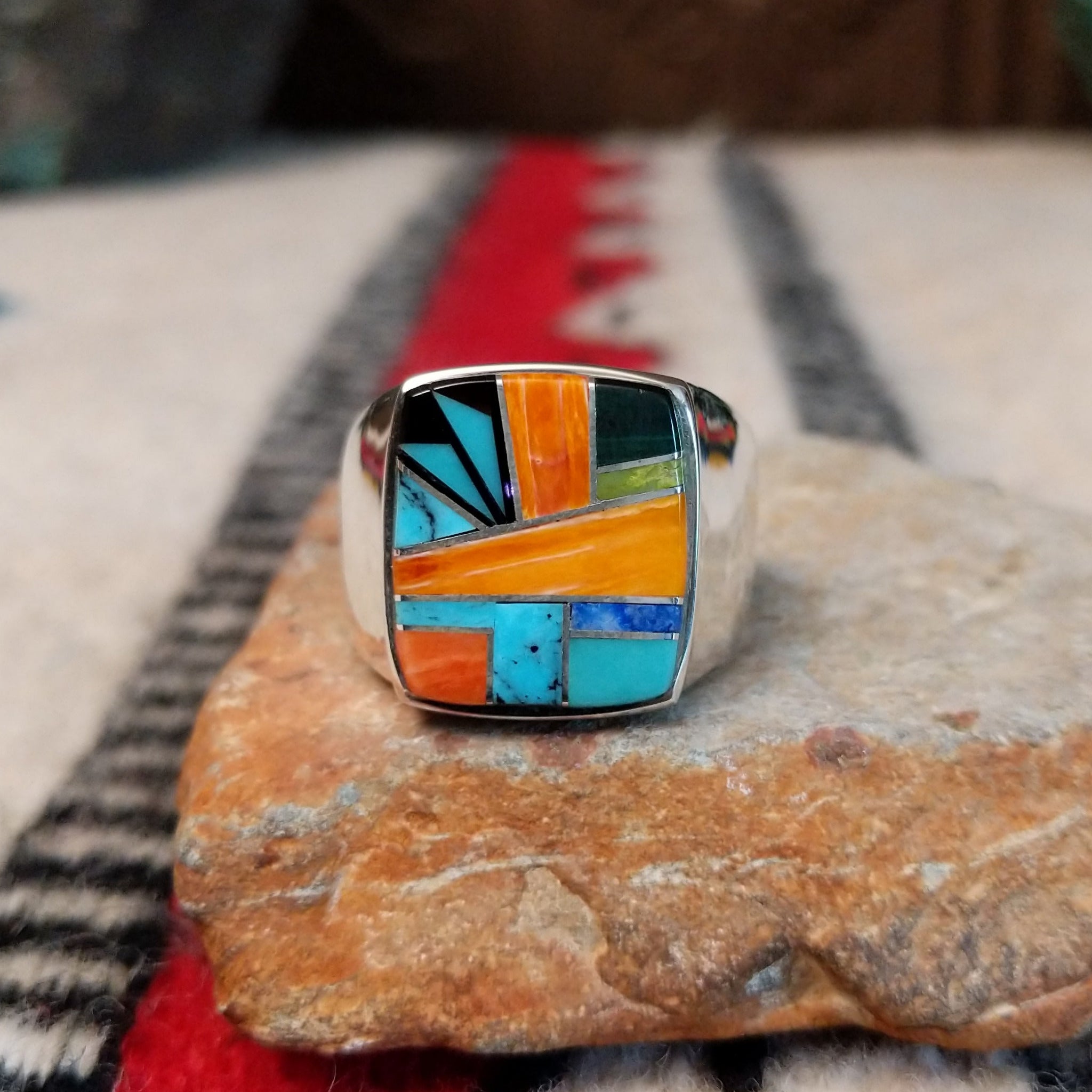 Navajo multistone inlay ring by O.J. featuring a rectangular geometric design with orange shell, turquoise, blue, green, and black inlay set in a polished silver band.