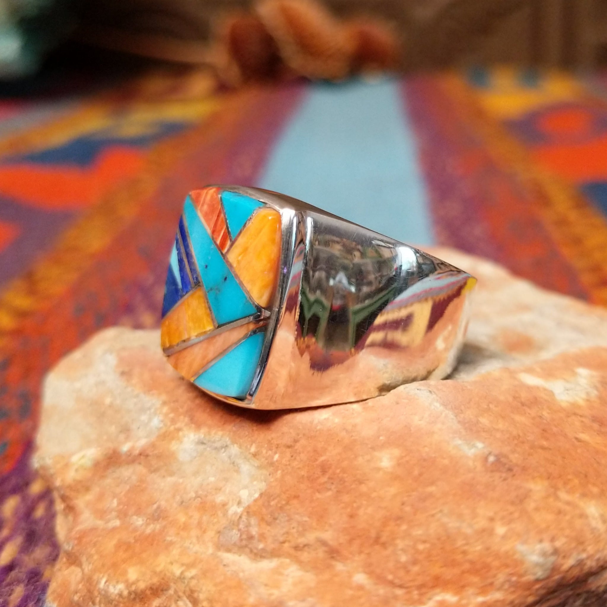 Navajo Multistone Inlay Ring by R.L. featuring geometric turquoise, lapis, and orange and red-toned spiney oyster shell inlay separated by Sterling Silver channels on a polished silver band; side view.