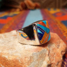 Navajo Multistone Inlay Ring by R.L. featuring geometric turquoise, lapis, and orange and red-toned spiney oyster shell inlay separated by Sterling Silver channels on a polished silver band; side view.