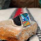 Navajo multistone inlay ring by V.Y. featuring a rectangular geometric design with turquoise, blue, purple, green, orange, and white inlay set in a wide polished silver band; side view.