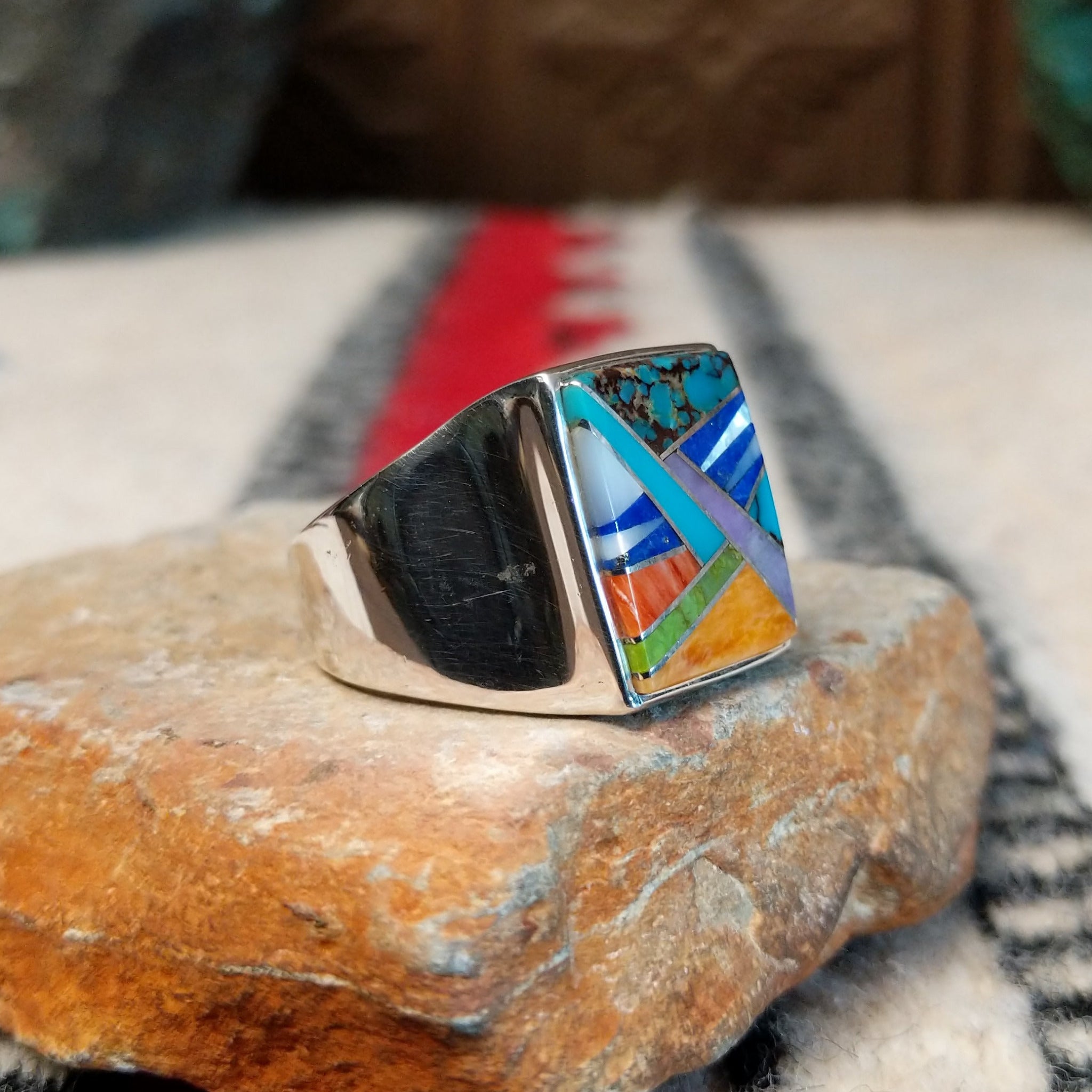 Navajo multistone inlay ring by V.Y. featuring a rectangular geometric design with turquoise, blue, purple, green, orange, and white inlay set in a wide polished silver band; side view.