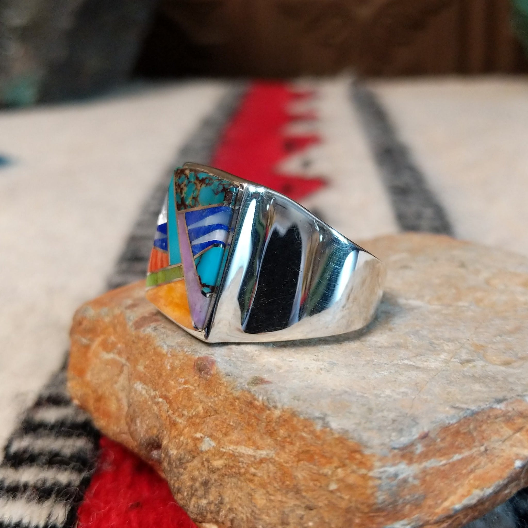 Navajo multistone inlay ring by V.Y. featuring a rectangular geometric design with turquoise, blue, purple, green, orange, and white inlay set in a wide polished silver band; side view.