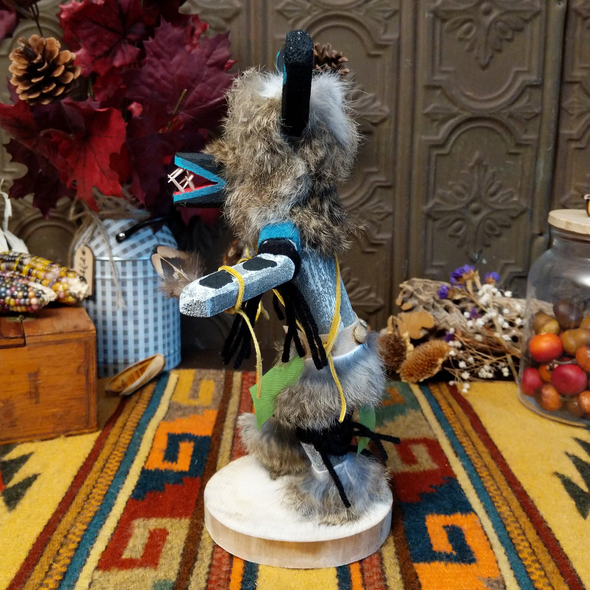 Side view of the Navajo Ogre Kachina doll with gray fur-covered face, black horns with turquoise markings, open red mouth, pointed teeth, and green fabric apron.
