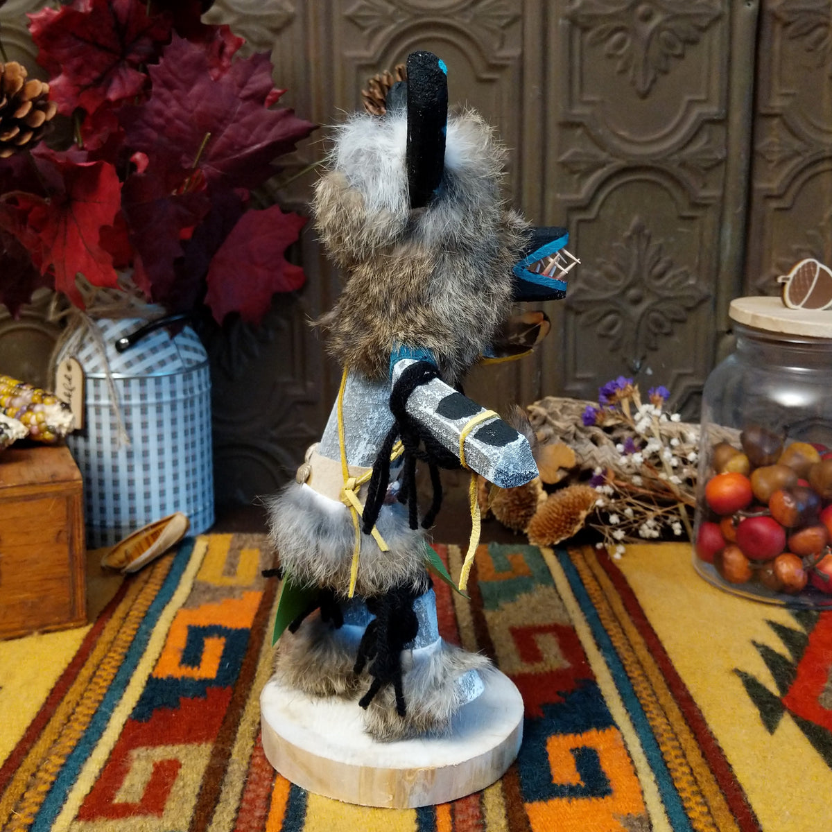 Side view of the Navajo Ogre Kachina doll with gray fur-covered face, black horns with turquoise markings, open red mouth, pointed teeth, and green fabric apron.