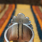 This elegant Navajo Ornate Sonoran Gold Turquoise Ring features a large oval blue turquoise stone surrounded by a silver rope border, polished silver beads, and decorative stamped silver blossoms; artisan stamp.